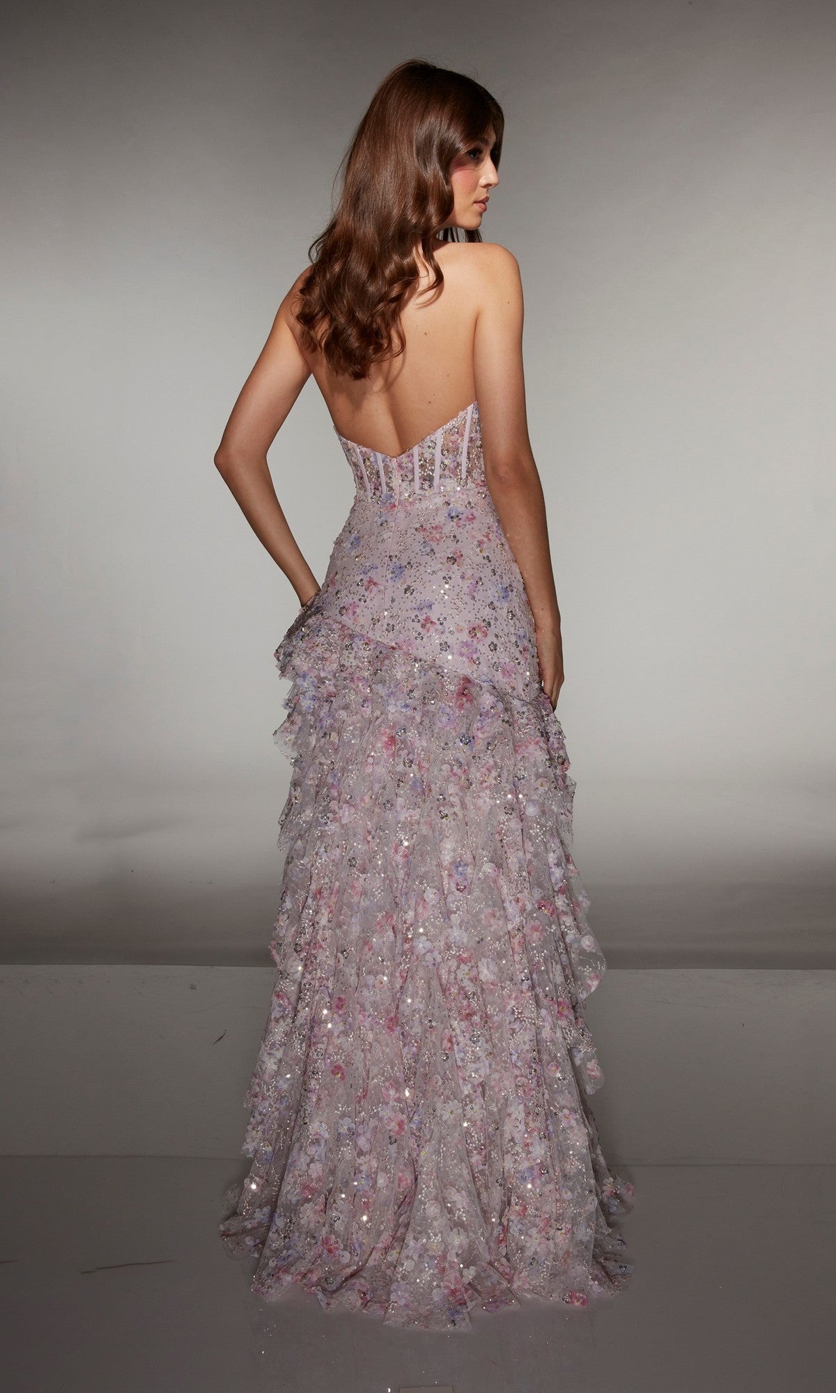 A woman faces away from the camera in the Alyce 61999 Long Prom Dress—a strapless, floor-length lavender floral gown featuring ruffles and a semi-sheer fitted corset bodice.